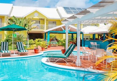 Vibrant pool area with striped lounge chairs, green umbrellas, and colorful tropical plants at Bay Gardens Hotel