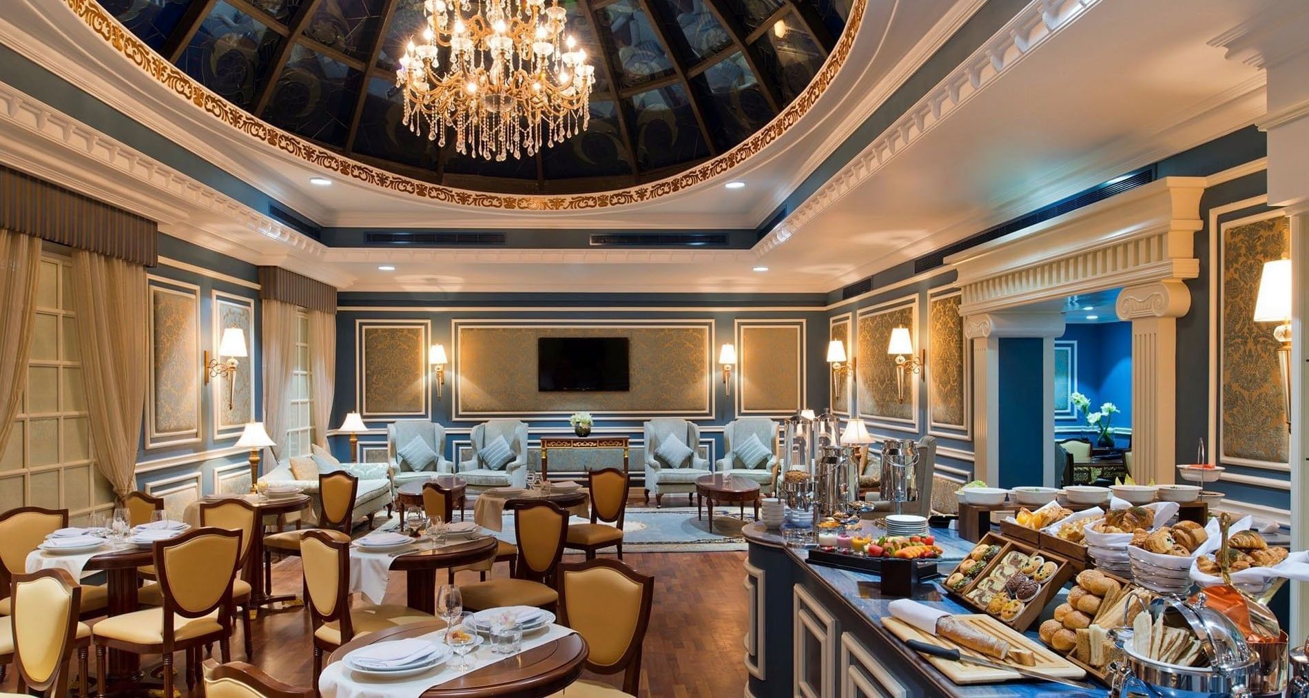 Elegant lounge featuring tan chairs by a breakfast buffet under a crystal chandelier in Coral Room at Warwick Doha Hotel