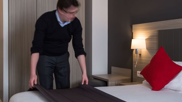 A man preparing a bed in a room at Hotel Marne-la-Vallee Est