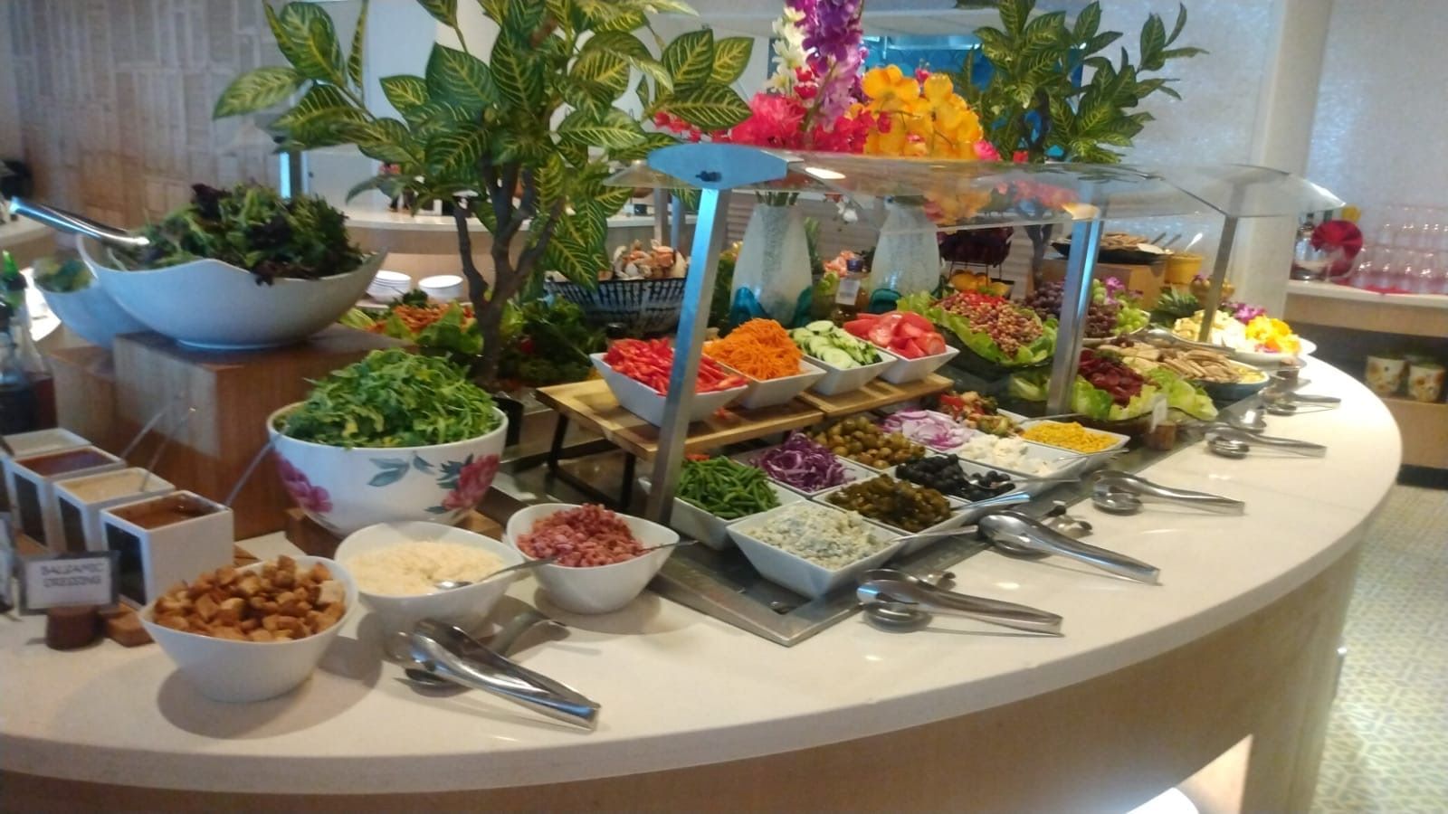 Buffet table with various salads, vegetables, and condiments, adorned with flowers and greenery.