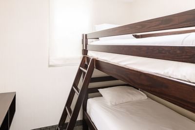 Wooden bunk beds with plush white pillows and built-in ladder by a bright window in the Royalty Family Suite at Rodd Royalty