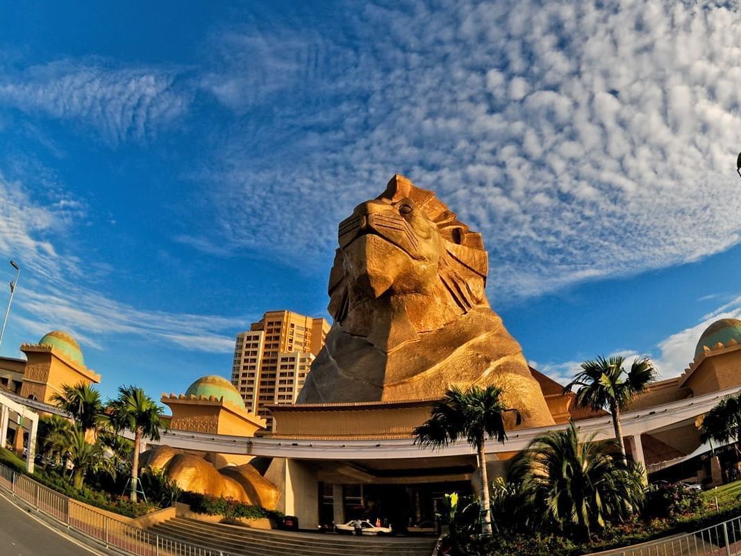 Lion statue towers over a vibrant complex under a blue sky, framed by palm trees near Saujana Hotel Kuala Lumpur
