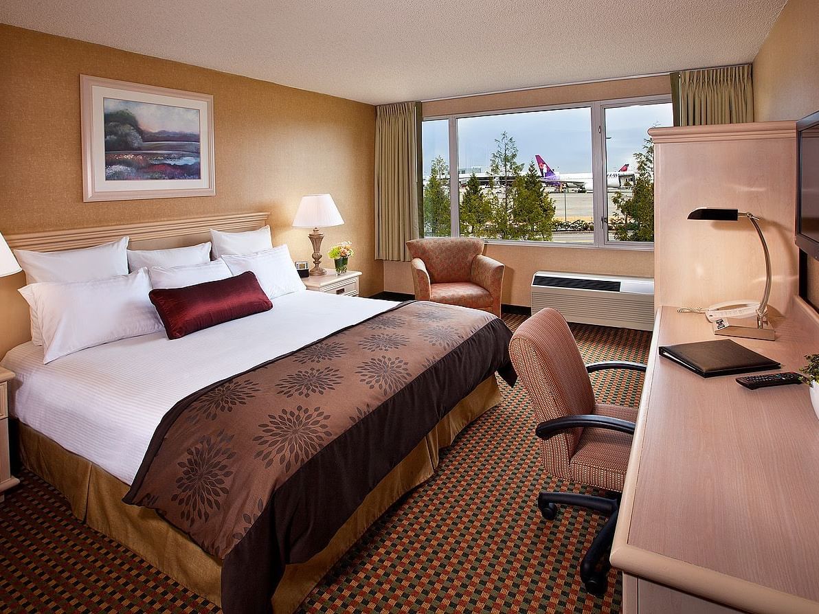 King bed and desk in hotel room with view of airport