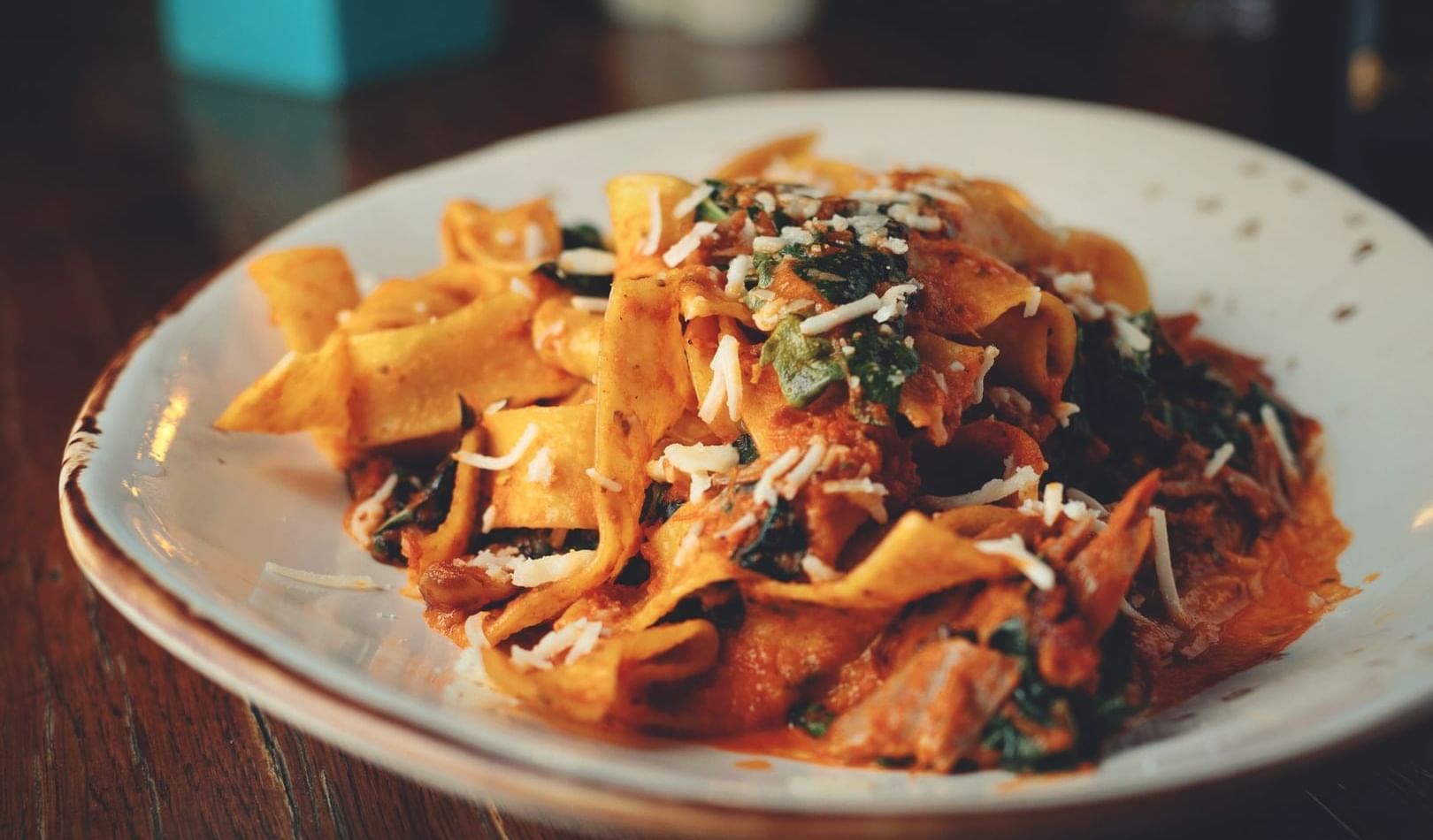 A plate of thick flat pasta noodes with red sauce and parmesan cheese