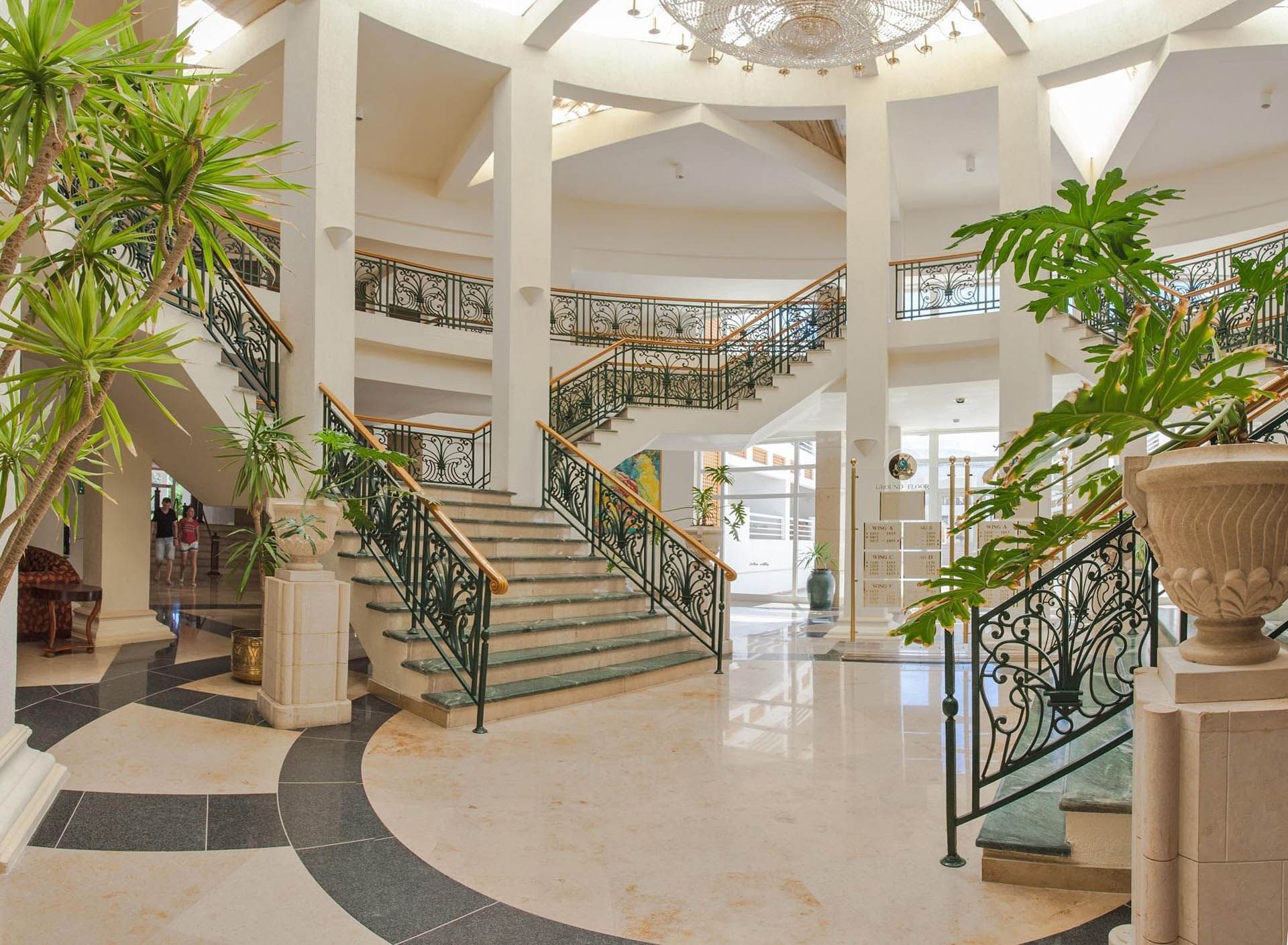 Lobby at Pickalbatros Golf Beach Resort with grand staircase, ornate railings, lush plants, and polished marble floors