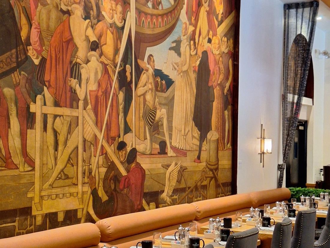 Long dining table with orange banquette seating positioned before large historical mural in Murals on 54 at Warwick New York