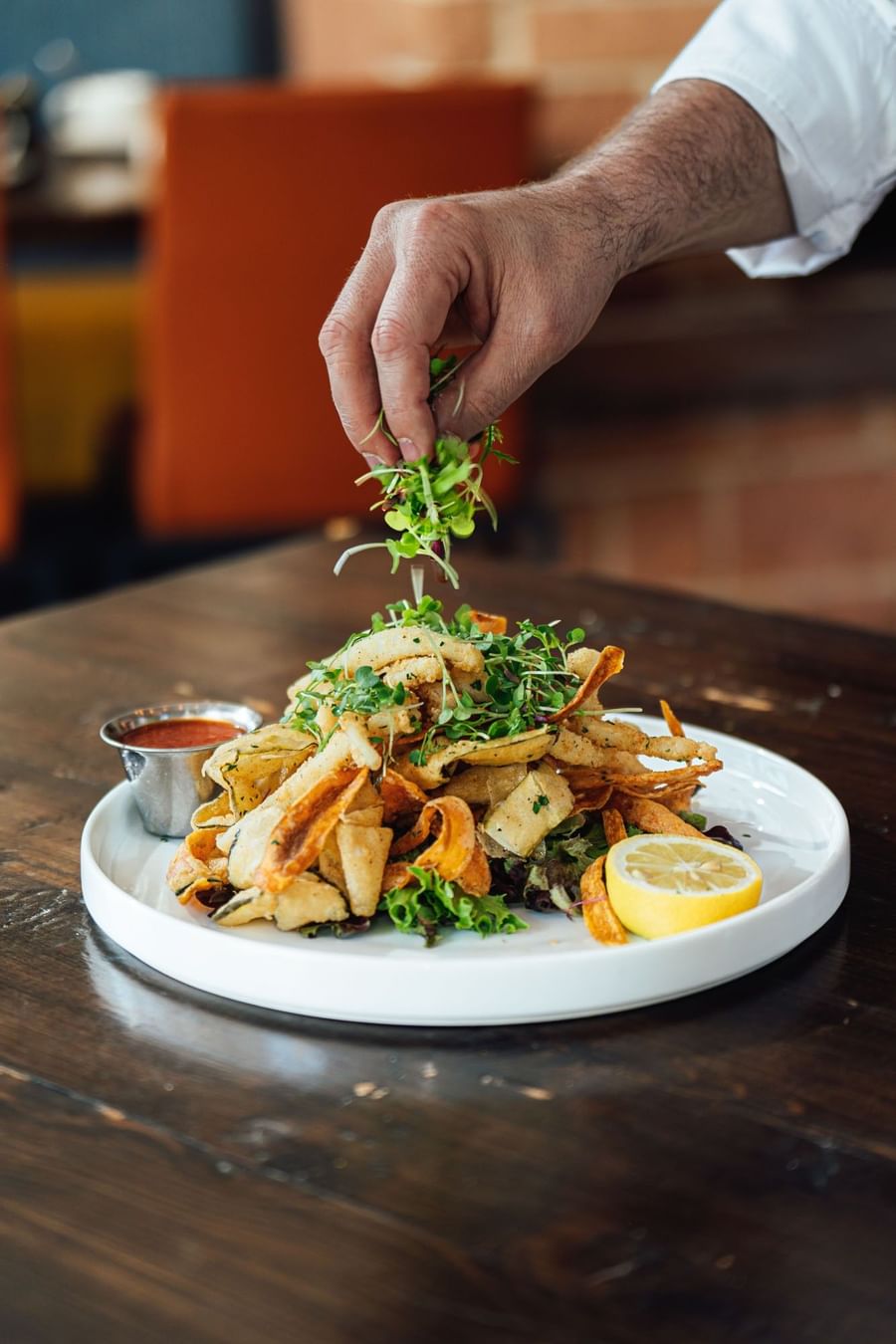 Hand adding microgreens over crispy calamari dish on a white plate at a table at Warwick Denver