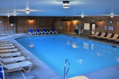 Fox Ridge Resort indoor pool with lounge chairs and a blue, tiled floor surrounded by wooden walls with clocks.