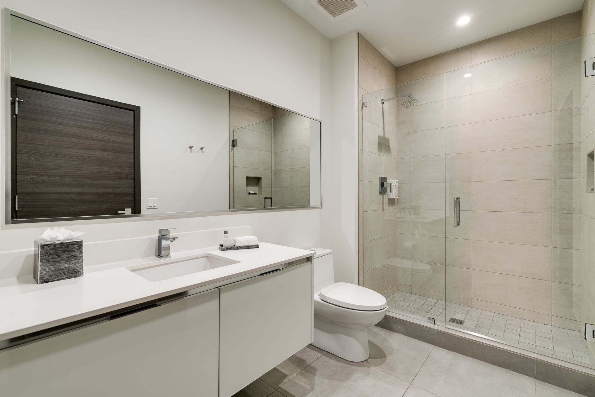 A modern bathroom with a tiled shower, glass shower door, sink, toilet, and mirror.