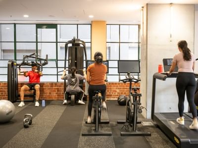 People exercising in a gym with various equipment including treadmills, weight machines, and free weights.
