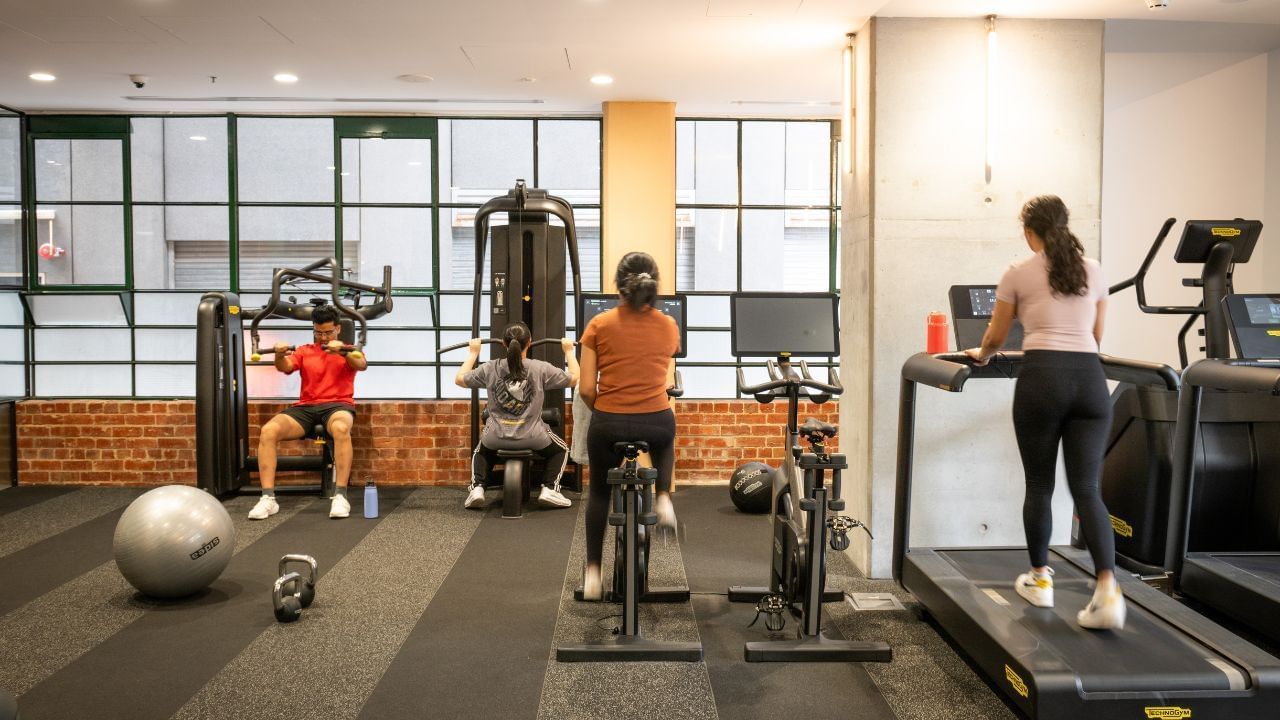 People exercising in a gym with various equipment including treadmills, weight machines, and free weights.