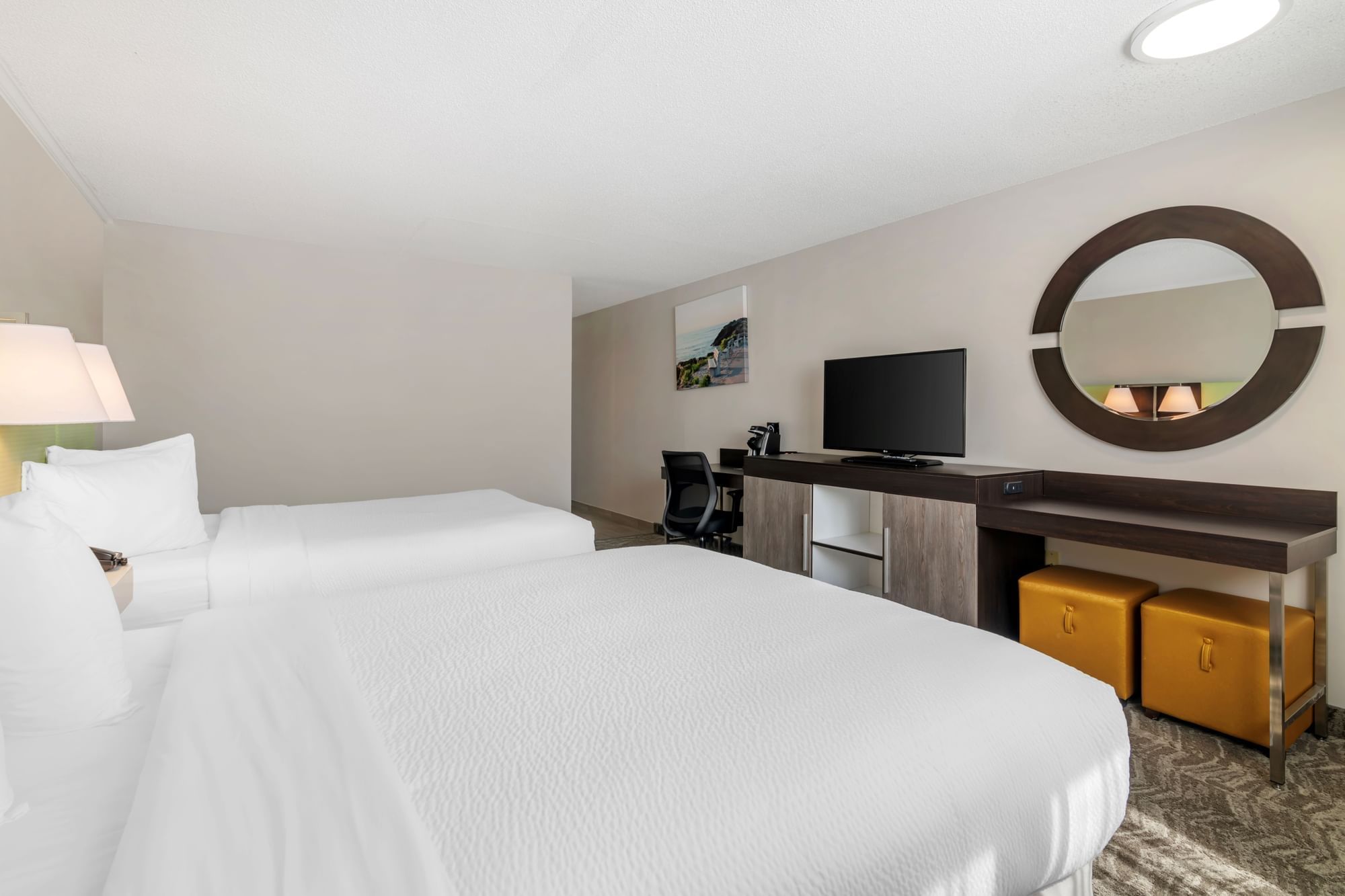 A hotel room with two queen beds, a desk, TV, and mirror.