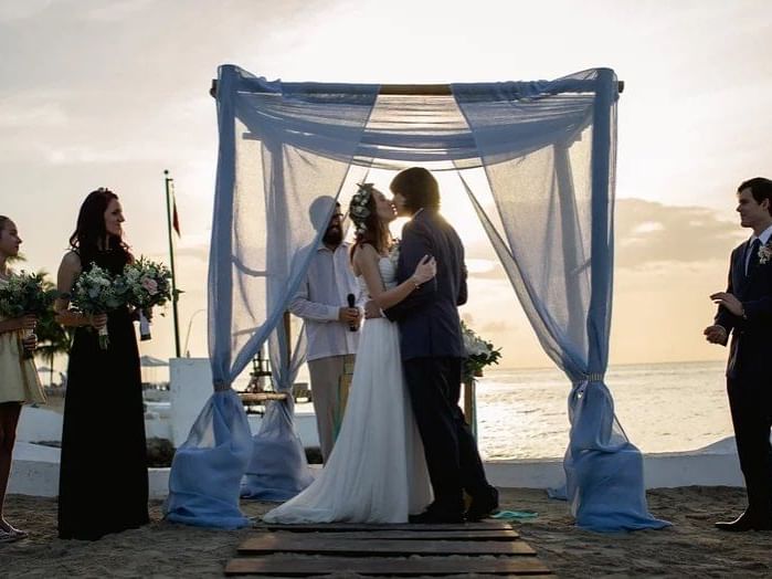 A bride and groom share a romantic kiss under a beautiful blue canopy on a picturesque beach at Live Aqua Beach Resort