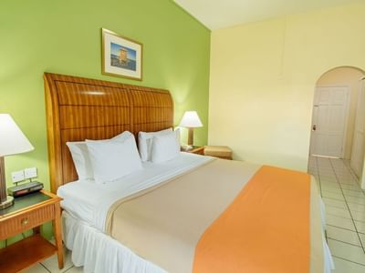 Cozy room with a wood-paneled bed, white linens, green walls, and a nightstand in Deluxe Room King at Bay Gardens Inn