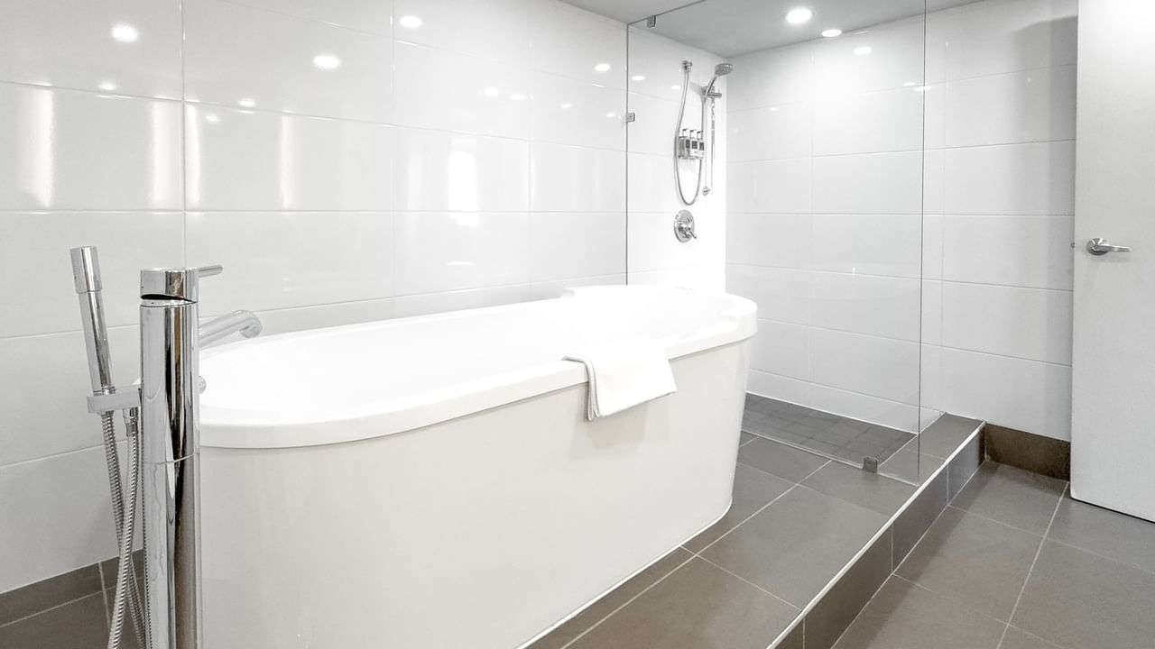 Modern white bathtub, towel, and glass shower enclosure in a hotel bathroom.