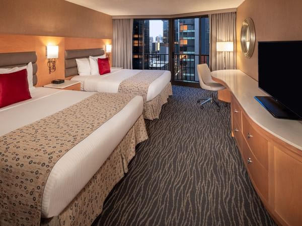 Two beds, desk, chair, TV, and balcony with city view