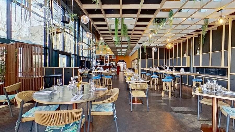 Intérieur d'un restaurant avec tables, chaises, plantes suspendues et verres sur les tables.