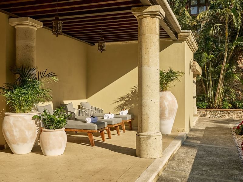 Shaded outdoor lounge area at Fiesta Americana, featuring comfortable daybeds, potted plants, and sturdy stone columns