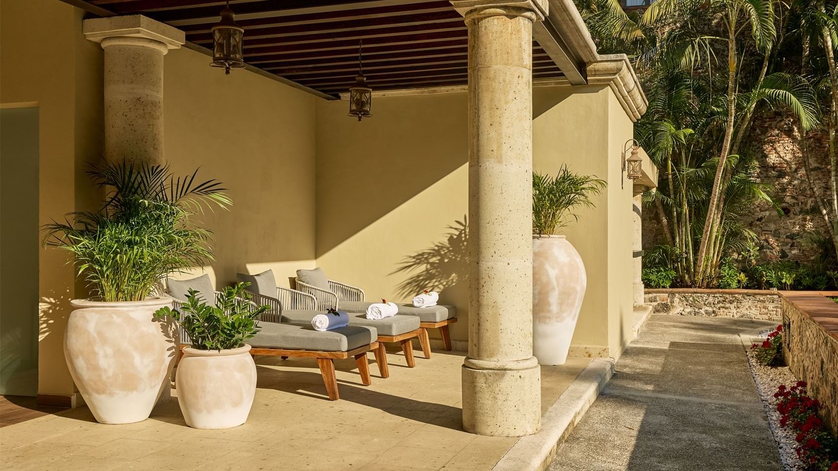 Shaded outdoor lounge area at Fiesta Americana, featuring comfortable daybeds, potted plants, and sturdy stone columns