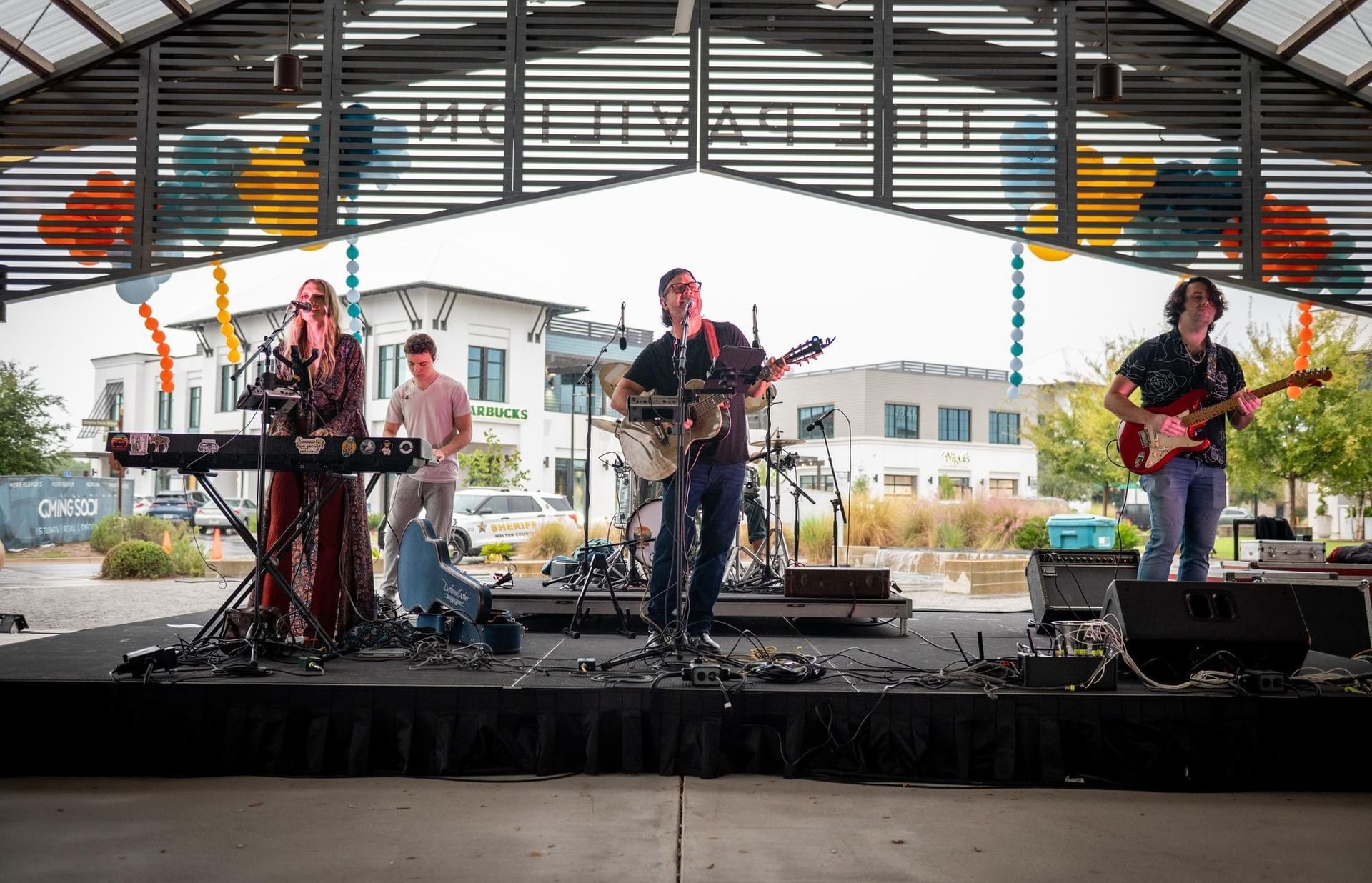 Live band performing on outdoor stage with colorful decorations under the Watersound Town Center pavilion.