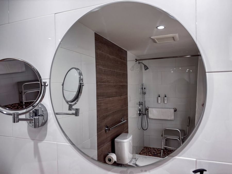 Round mirror reflecting an accessible shower with a bench in Island View Accessible at Warwick Paradise Island Bahamas