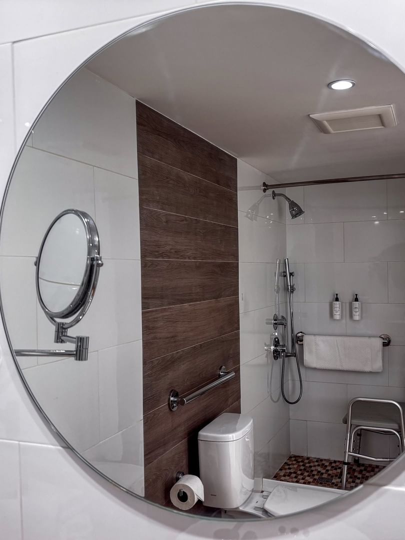 Round mirror reflecting an accessible shower with a bench in Island View Accessible at Warwick Paradise Island Bahamas