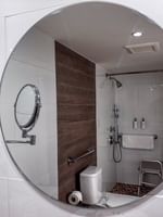 Round mirror reflecting an accessible shower with a bench in Island View Accessible at Warwick Paradise Island Bahamas