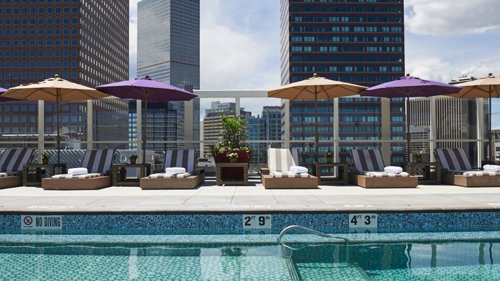 Poolside lounge chairs with colorful umbrellas placed by a tiled pool at Warwick Grand Place Brussels