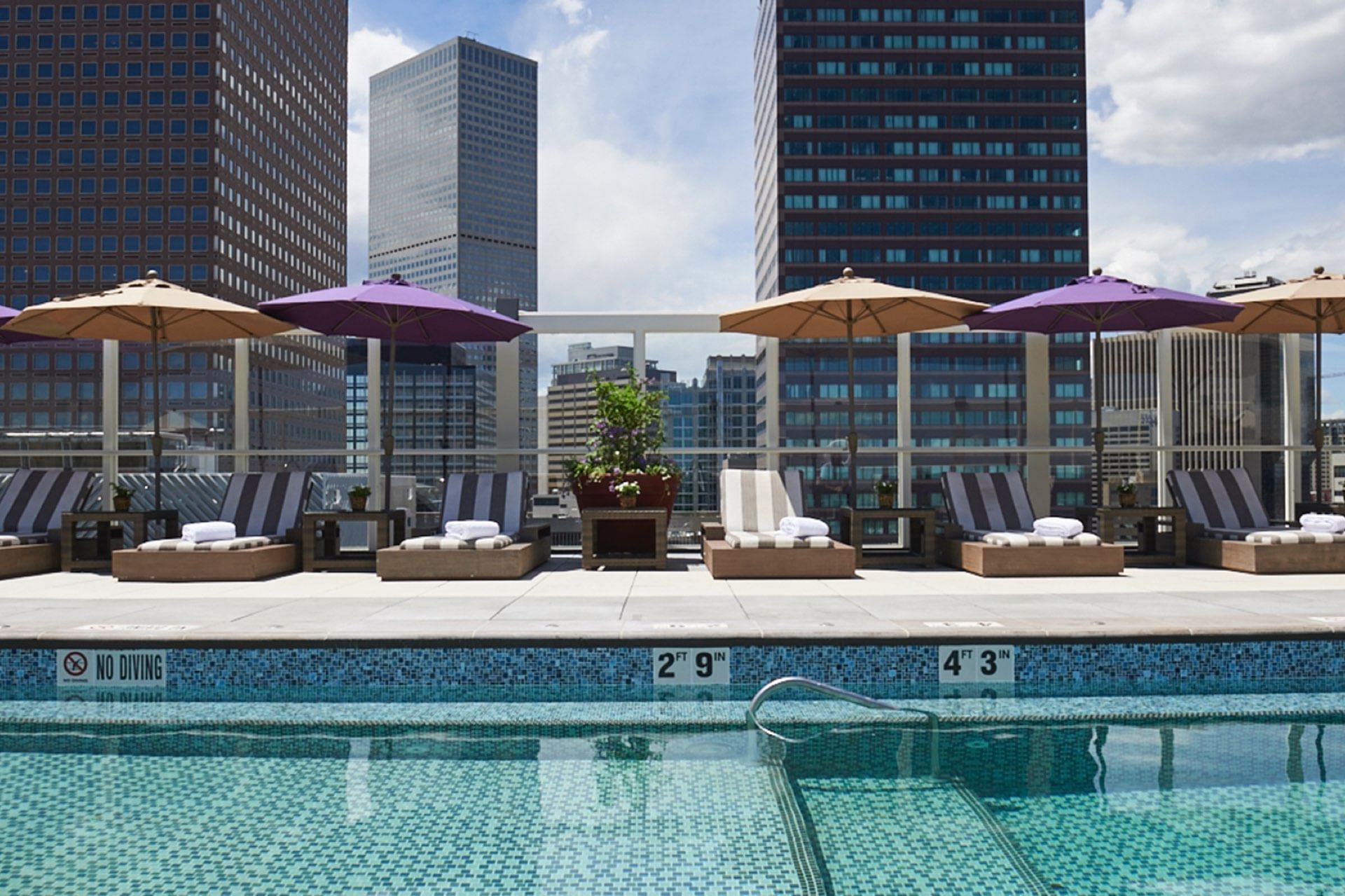 A rooftop pool with lounge chairs and umbrellas overlooking the city skyline.