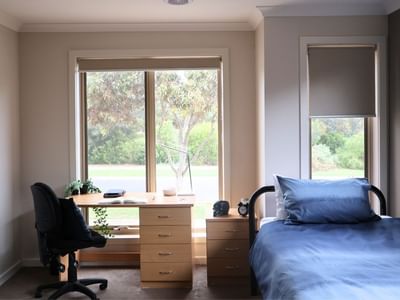 Cozy room with bed, desk, chair, and scenic window view at La Trobe University Regional Housing Melton.
