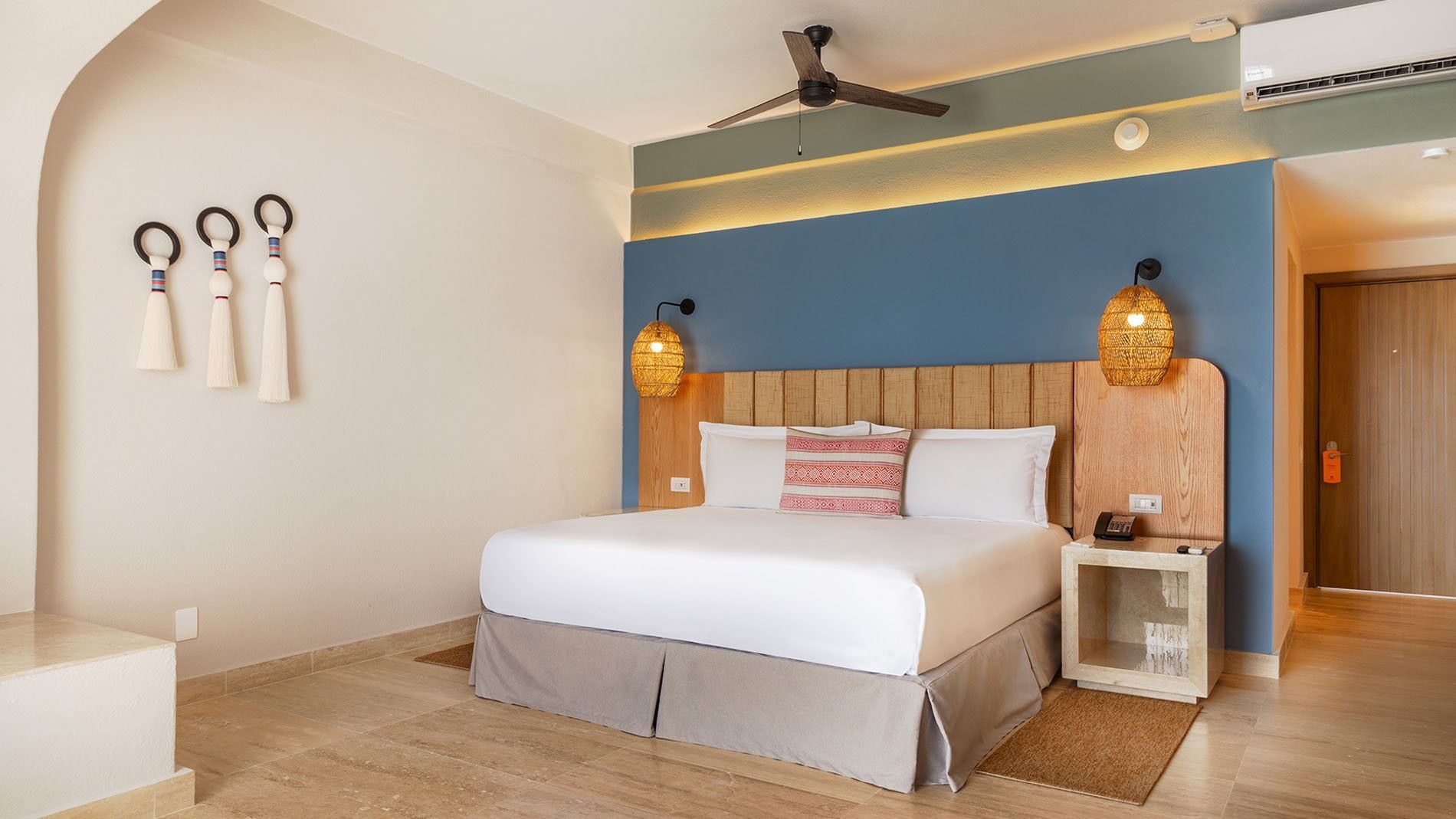 King Camino Real Club king bed with blue accent wall and woven pendant lighting at Camino Real Acapulco Diamante