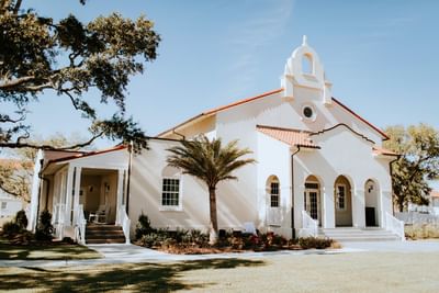 Historic, white stucco The Chapel with a Spanish Colonial arch, red tile roof, and a palm tree near Centennial Plaza Resort