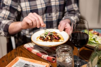 Person dining with a slice of pizza and a glass of wine in The Lodge at Schroon Lake