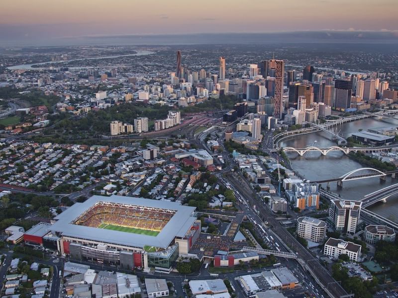 Aerial view of Brisbane's city skyline, river, bridges, and Suncorp Stadium full of fans at sunset near The Sebel Brisbane