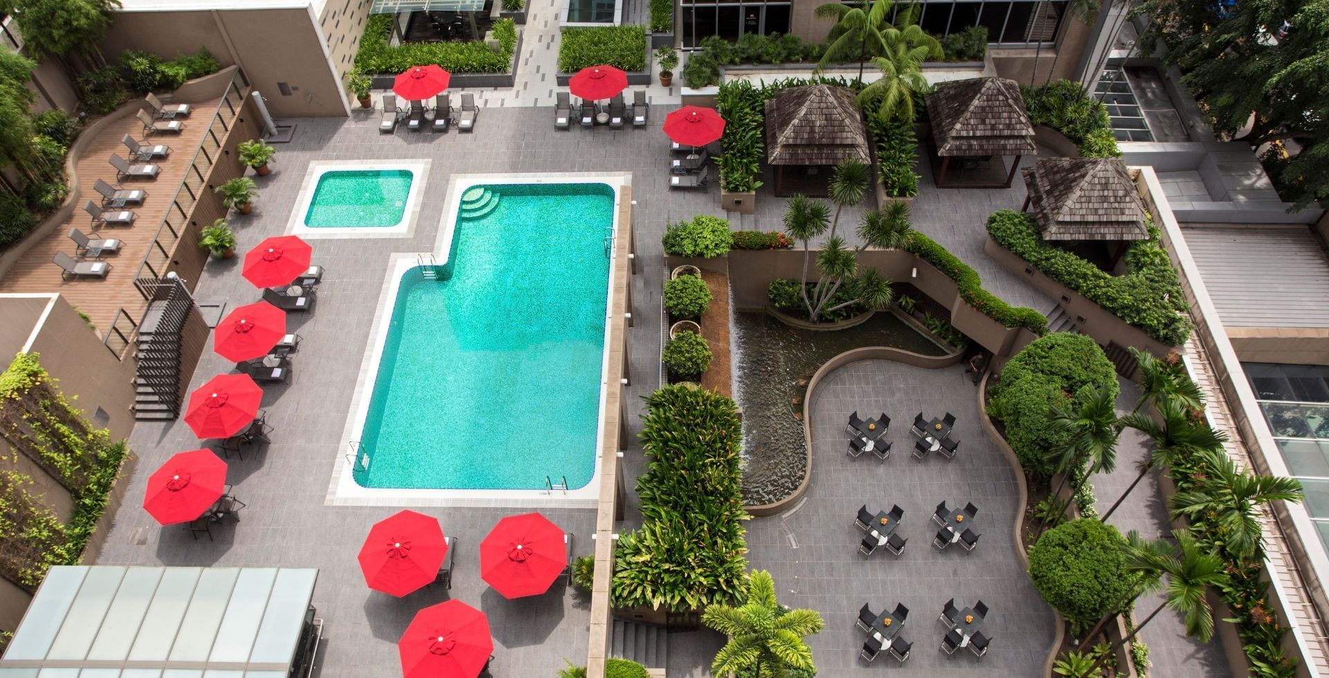 An aerial view of the outdoor pool area with bright red umbrellas and lush greenery at Carlton Hotel Singapore