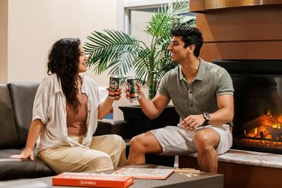 Couple by a fireplace in a lounge under a palm tree at Rodd Brudenell River Resort, one of the premier places to stay in PEI