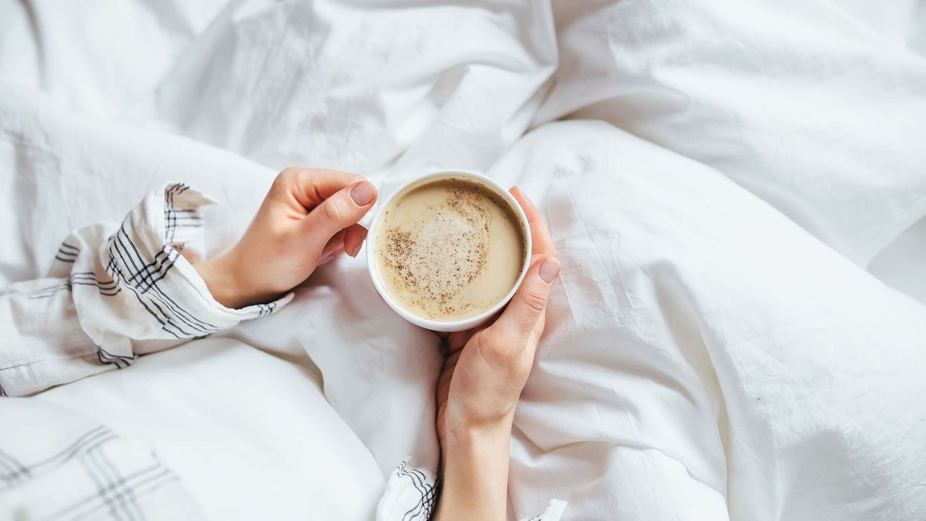 Guest in bed with patterned sleeves holding a white cup of coffee at The Capital Hotel, Apartments and Townhouse