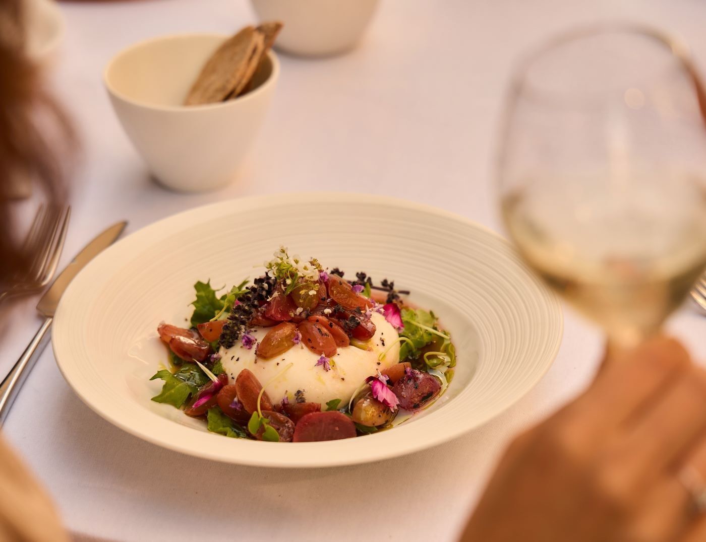 Salade gastronomique à la burrata, aux raisins, aux légumes verts et aux fleurs comestibles, servie dans une assiette blanche au restaurant The Londoner