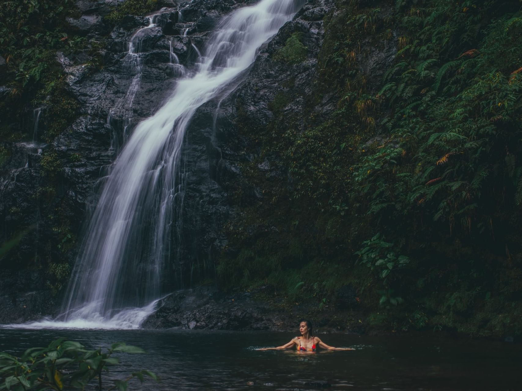 Lady swimming in a forest pool at the base of a flowing waterfall near El Silencio Lodge and Spa