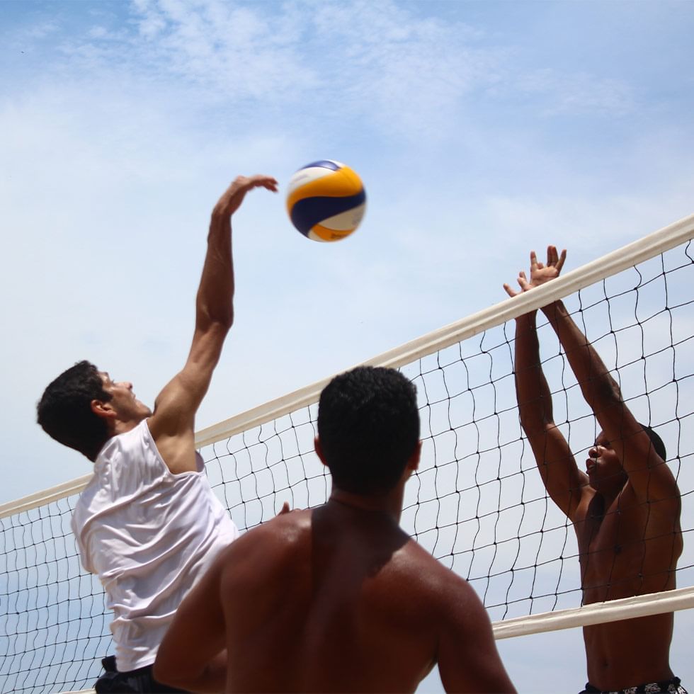 Drei Männer spielen Volleyball an einem Netz unter einem blauen Himmel.