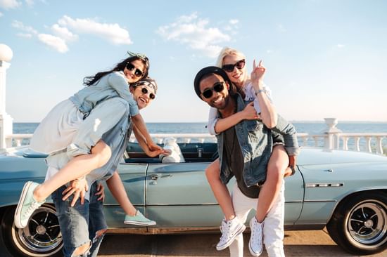 Two couples smiling next to retro blue car with ocean view