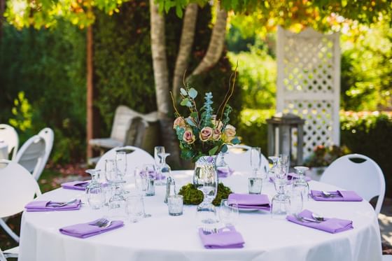 Outdoor reception table with white linens, purple napkins, rose centerpiece, and garden setting at Cambria Pines Lodge