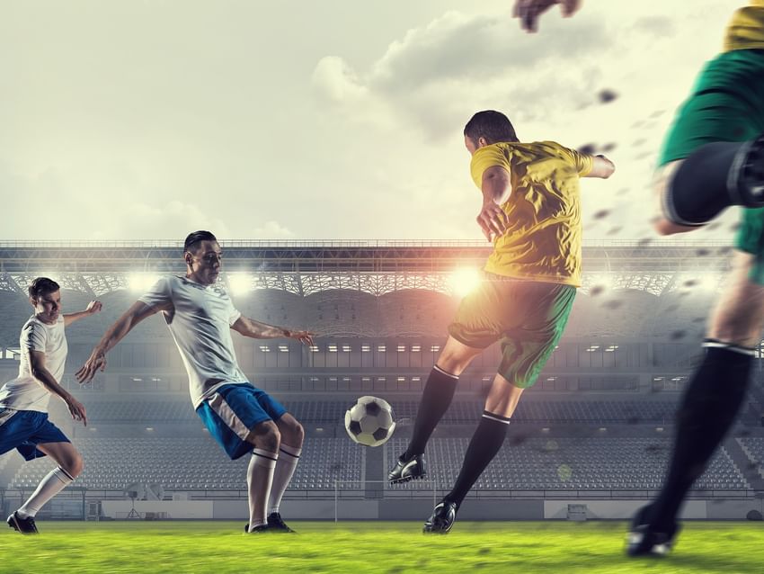 Futbolistas profesionales en acción sobre un amplio campo verde en un gran estadio al atardecer cerca de Camino Real
