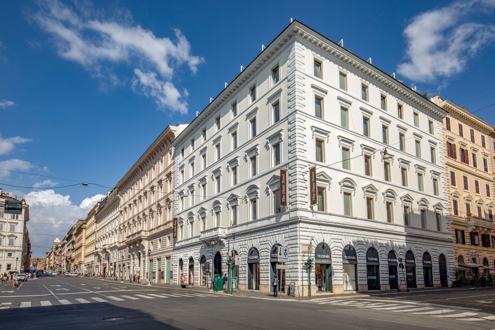Low-angle exterior view of The Glam Hotel with street view on a sunny day