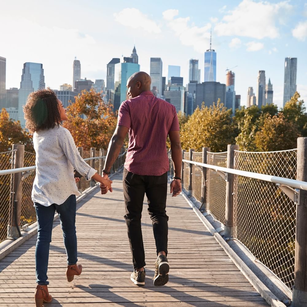 Couple holding hands on a wooden bridge by metal railings, surrounded by fall foliage near Warwick New York