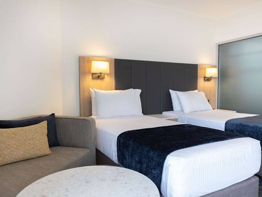 Two beds with side lamps and nearby sofas in Family Room at Hotel Grand Chancellor Brisbane