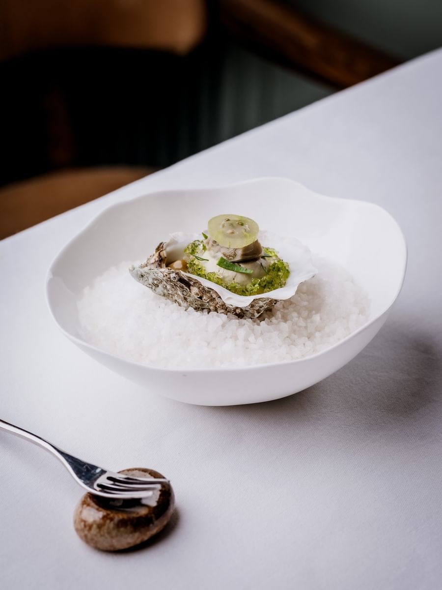 Oyster topped with green garnish and fruit slice resting in a bowl of ice at The Capital Hotel, Apartments and Townhouse