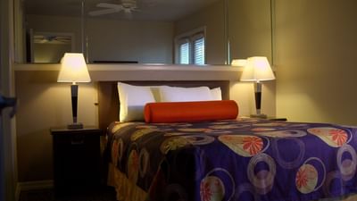 Guest room with colorful patterned bedding, orange bolster pillow, and matching bedside lamps at London Bridge Resort