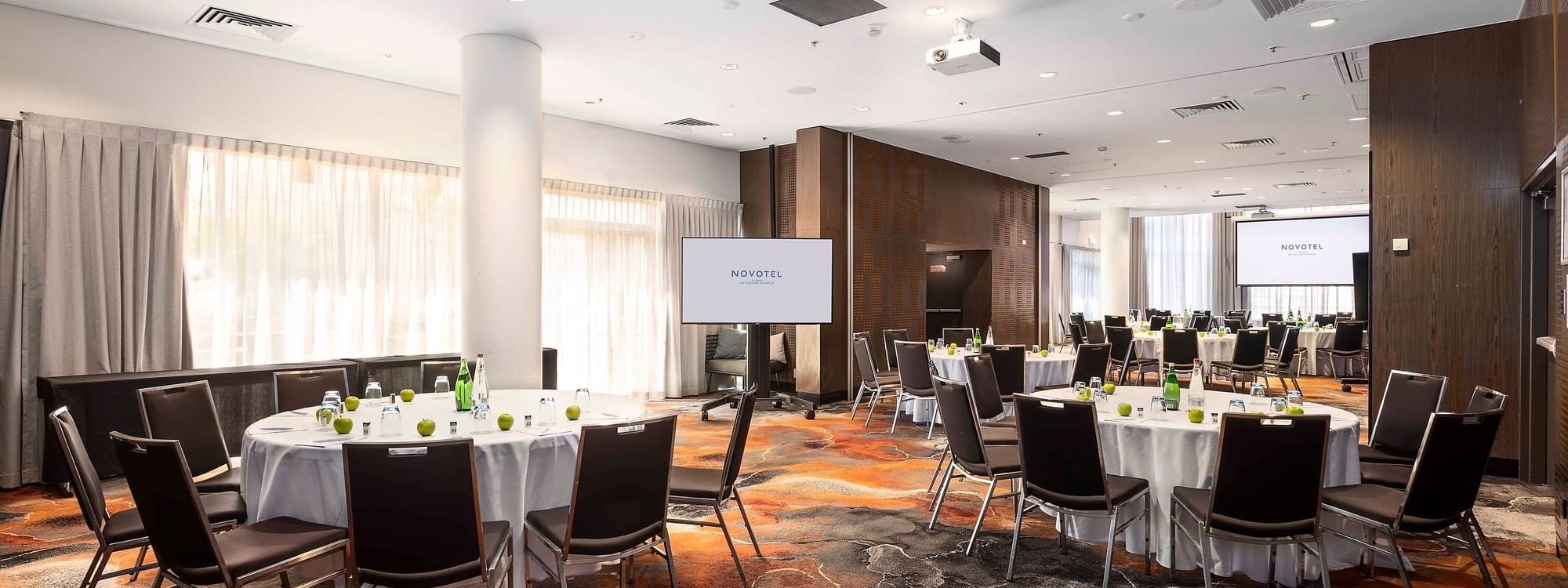 Banquets set up facing the projector screen in Hunter Room 1-4 at Novotel Sydney on Darling Harbour