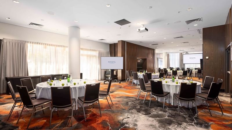 Banquets set up facing the projector screen in Hunter Room 1-4 at Novotel Sydney on Darling Harbour